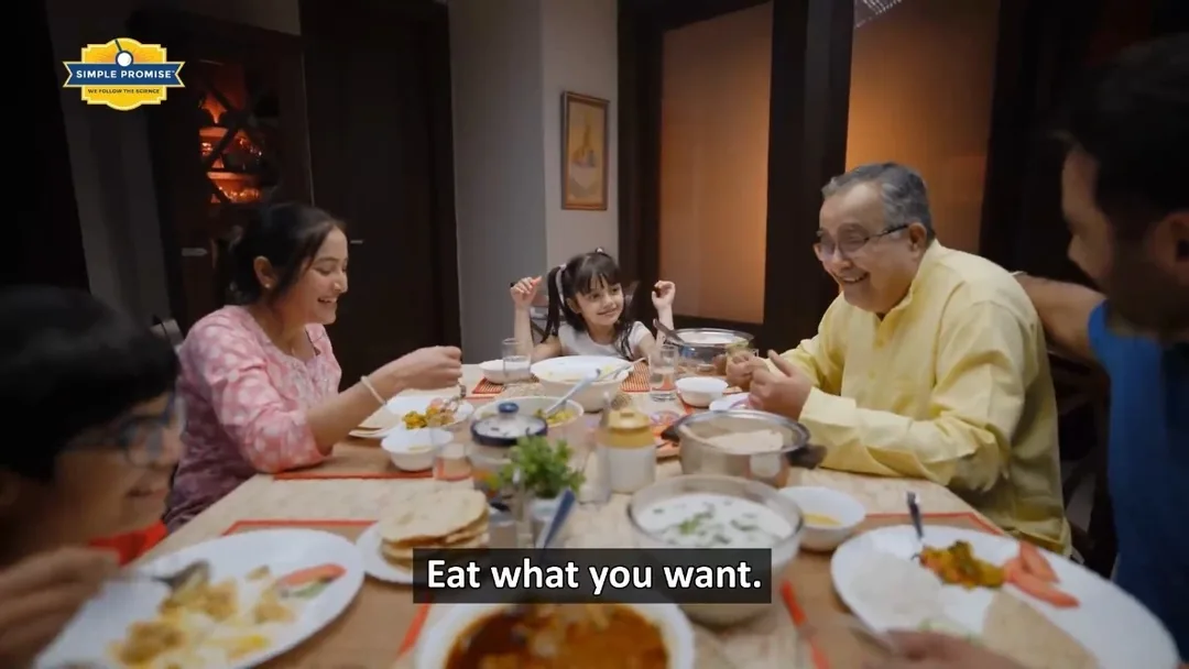 A still from the manufacturer's promotional video showing a family at dinner with the caption Eat what you want